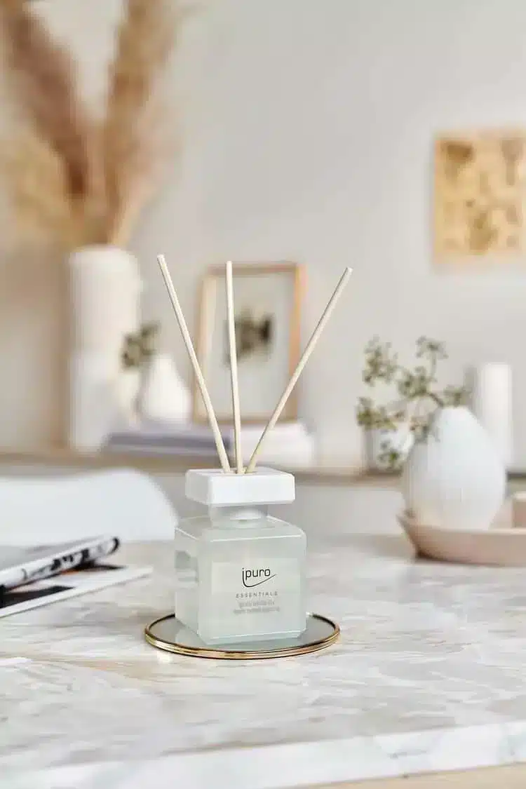 Ipuro Essentials White Lily Duftstäbchen in weißem Fläschchen auf Marmortisch mit Vasen im Hintergrund