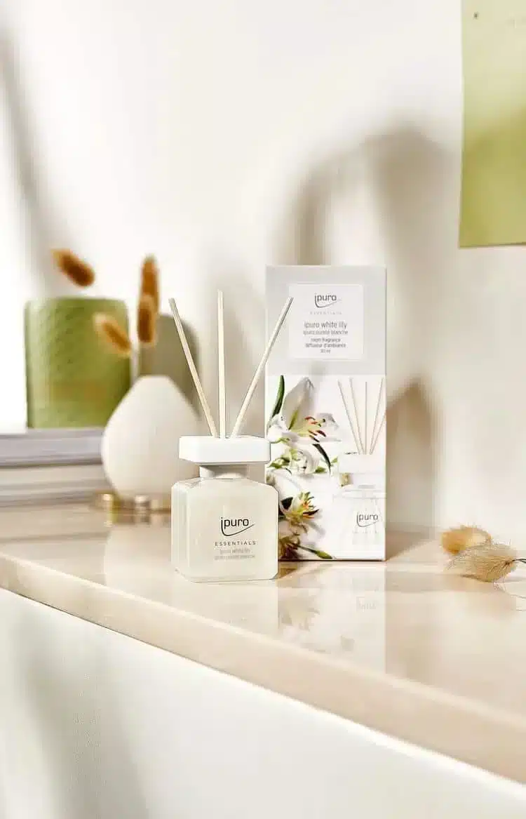 Ipuro Essentials White Lily Duftstäbchen neben Verpackung mit Lilienmuster auf hellem Regal